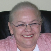 Dorota Grzywna, uśmiechnięta blondynka w średnim wieku, okulary w delikatnych oprawkach, różowa marynarka.