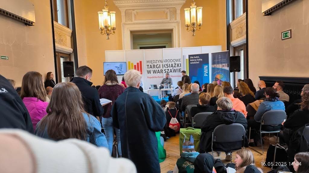 Grupa słuchaczy w Sali Mikołajskiej Pałacu Kultury patrzy na scenę z czwórką panelistów.