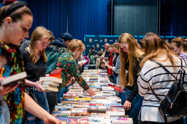 grupa osób po obu stronach zasłanego książkami stołu