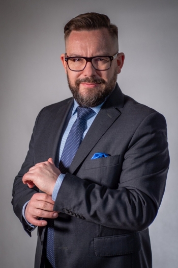 Jerzy Woźniakiewicz, elegancki mężczyzna w garniturze w okularach i brodzie patrzy na wprost