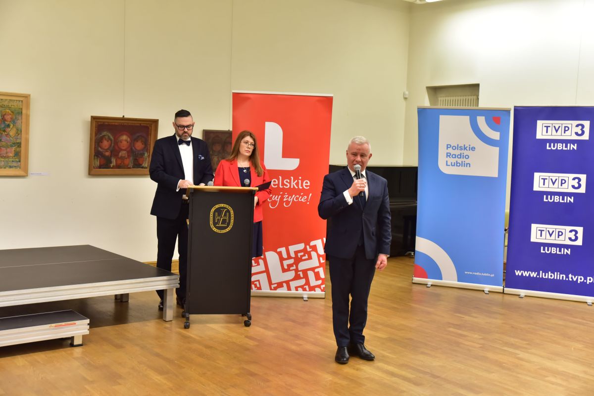 Ubrany w garnitur mężczyzna otwiera konferencję, w tle banery TVP 3 Lublin, Polskie Radio Lublin i województwa lubelskiego